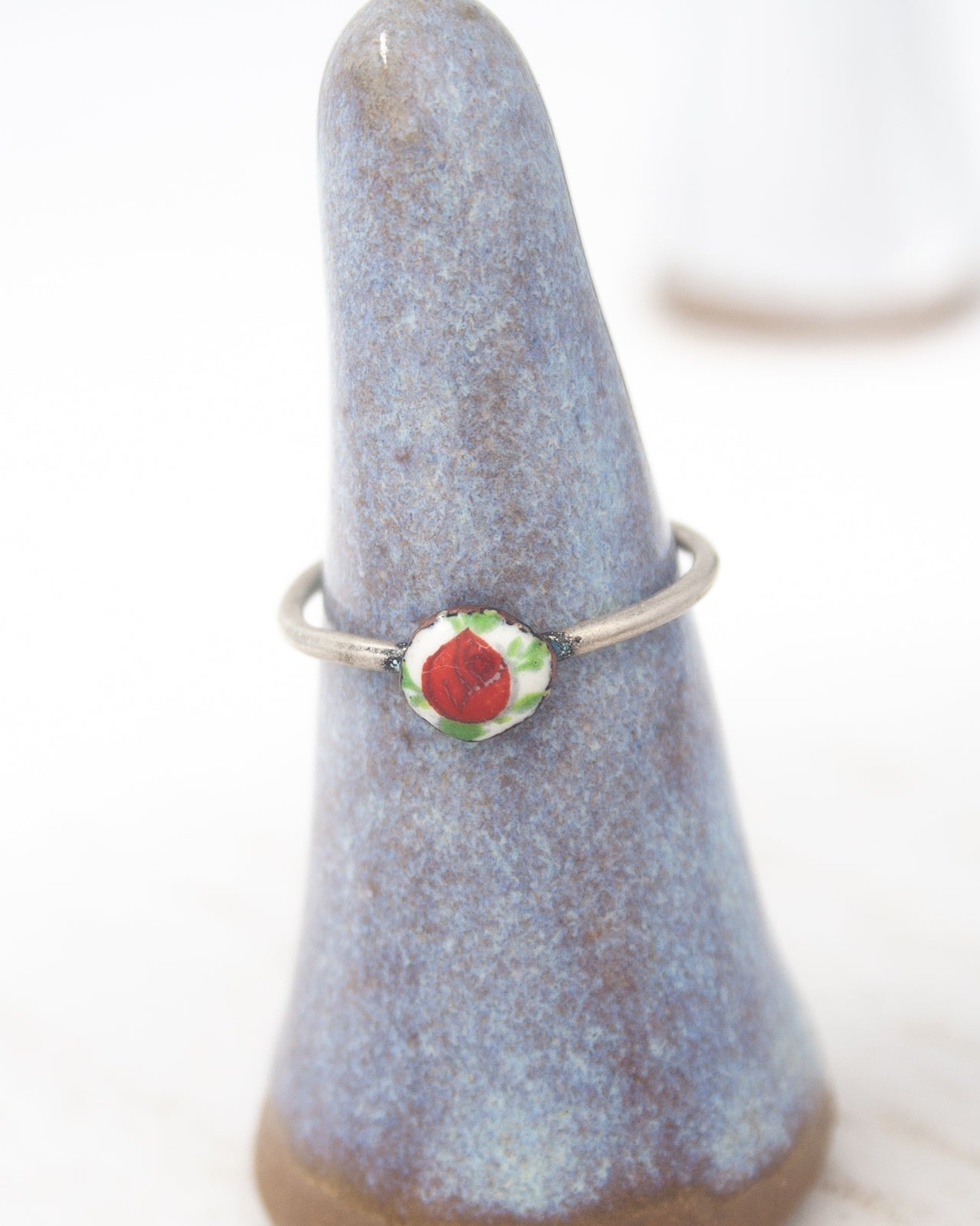 A ring with a red flower design is displayed on a blue ceramic stand.