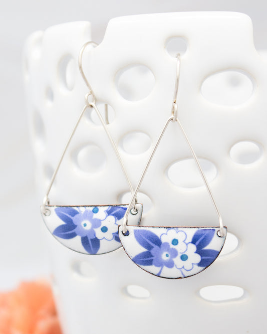 A pair of earrings with blue and white floral designs hanging from a white perforated holder.