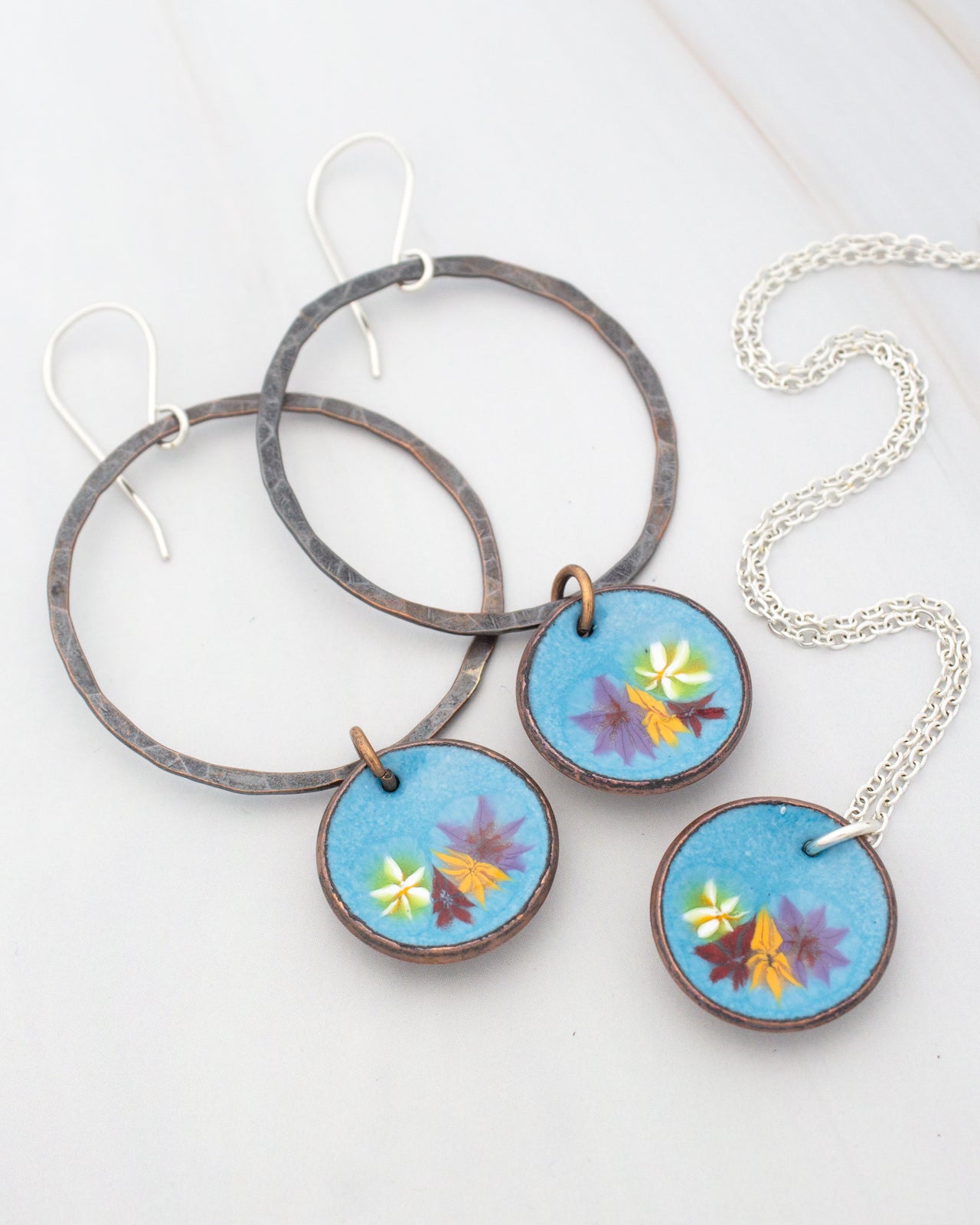 a pair of earrings and a necklace with blue and purple floral designs.