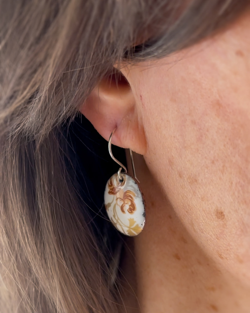A close-up view of a person's ear wearing a pair of earrings with a floral design.