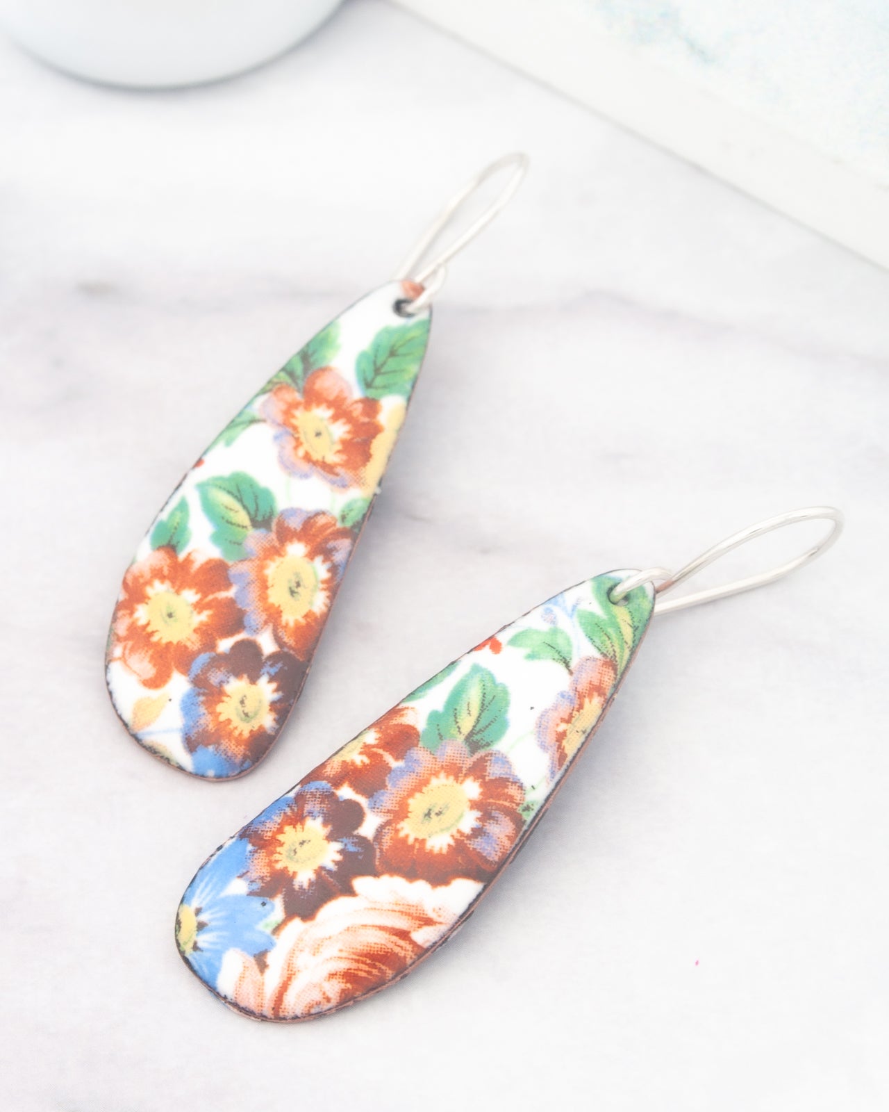 a pair of colorful earrings with floral designs, placed on a marble surface.
