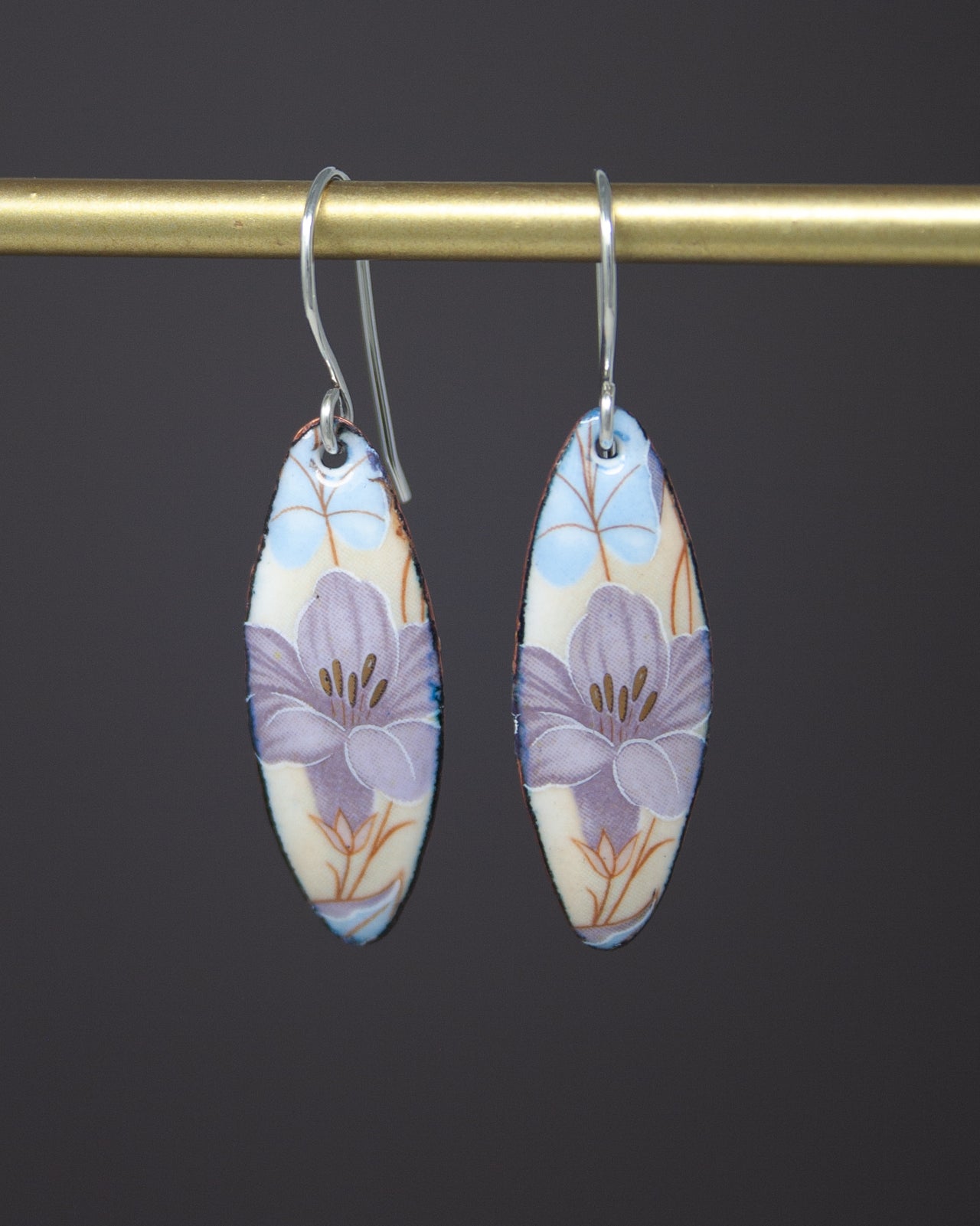 A pair of earrings with a floral design, featuring two oval-shaped pendants hanging from a gold-colored metal bar.