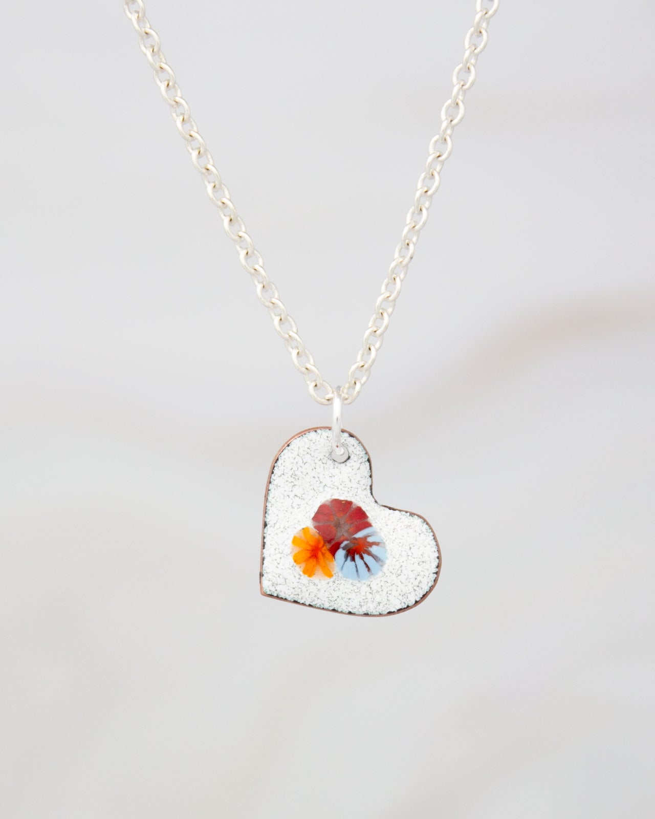 A silver necklace with a heart-shaped pendant featuring a colorful flower design.