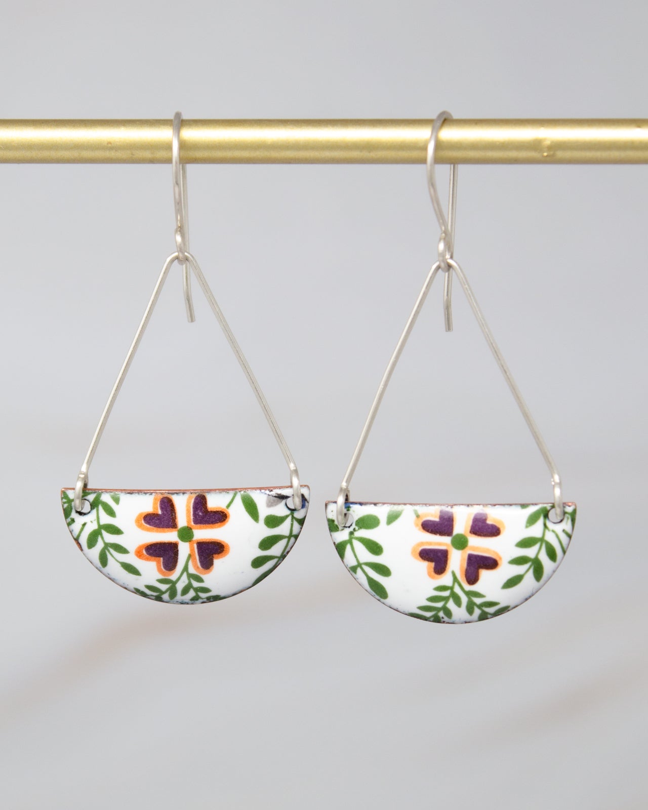 A pair of earrings with a floral design on the lower half, hanging from a gold-colored metal hook.