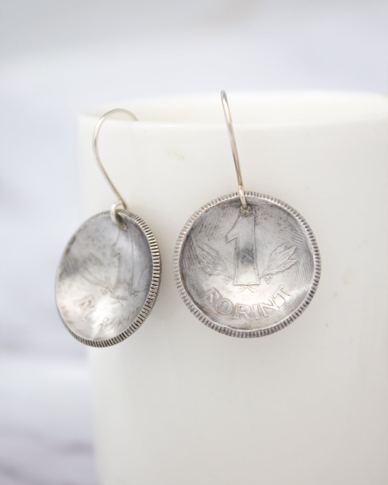 a pair of silver earrings with a coin-like design, hanging from a hook.