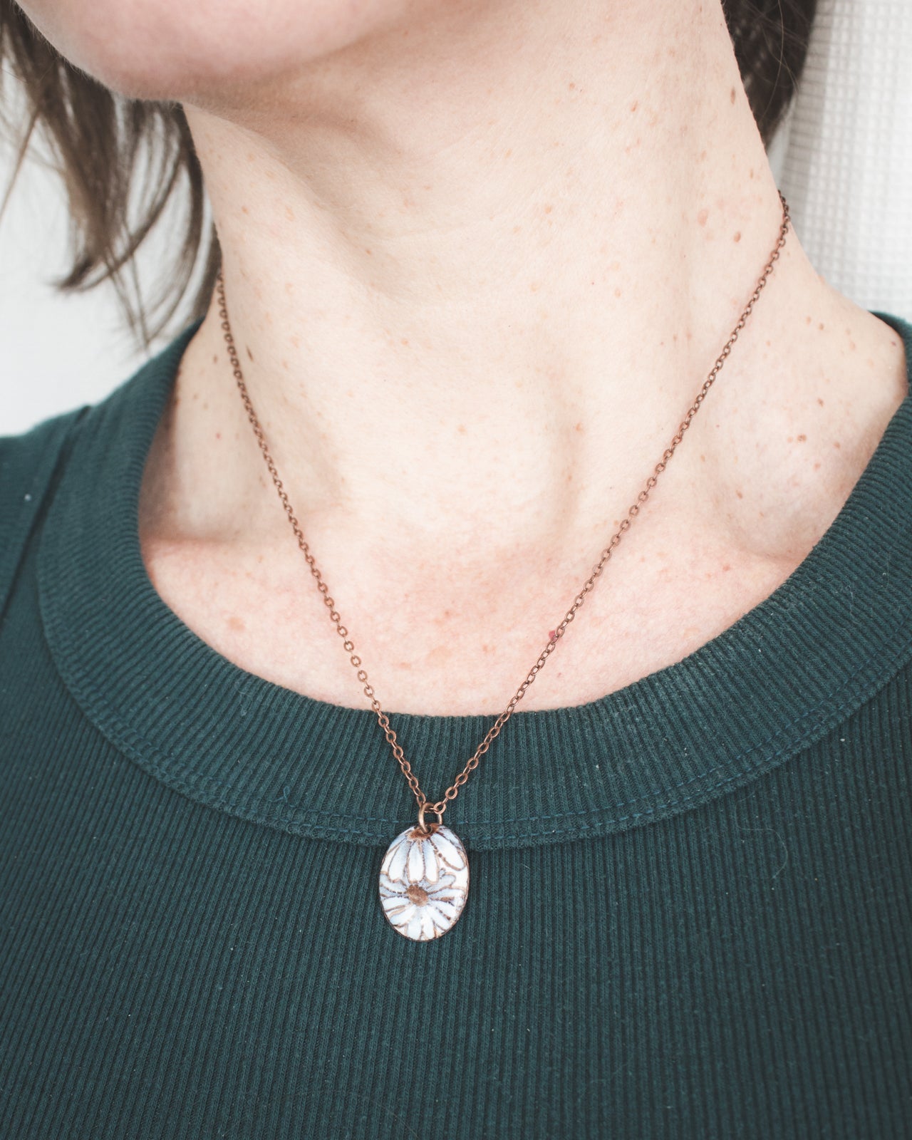 A woman wearing a green sweater and a necklace with a pendant is shown in the image.