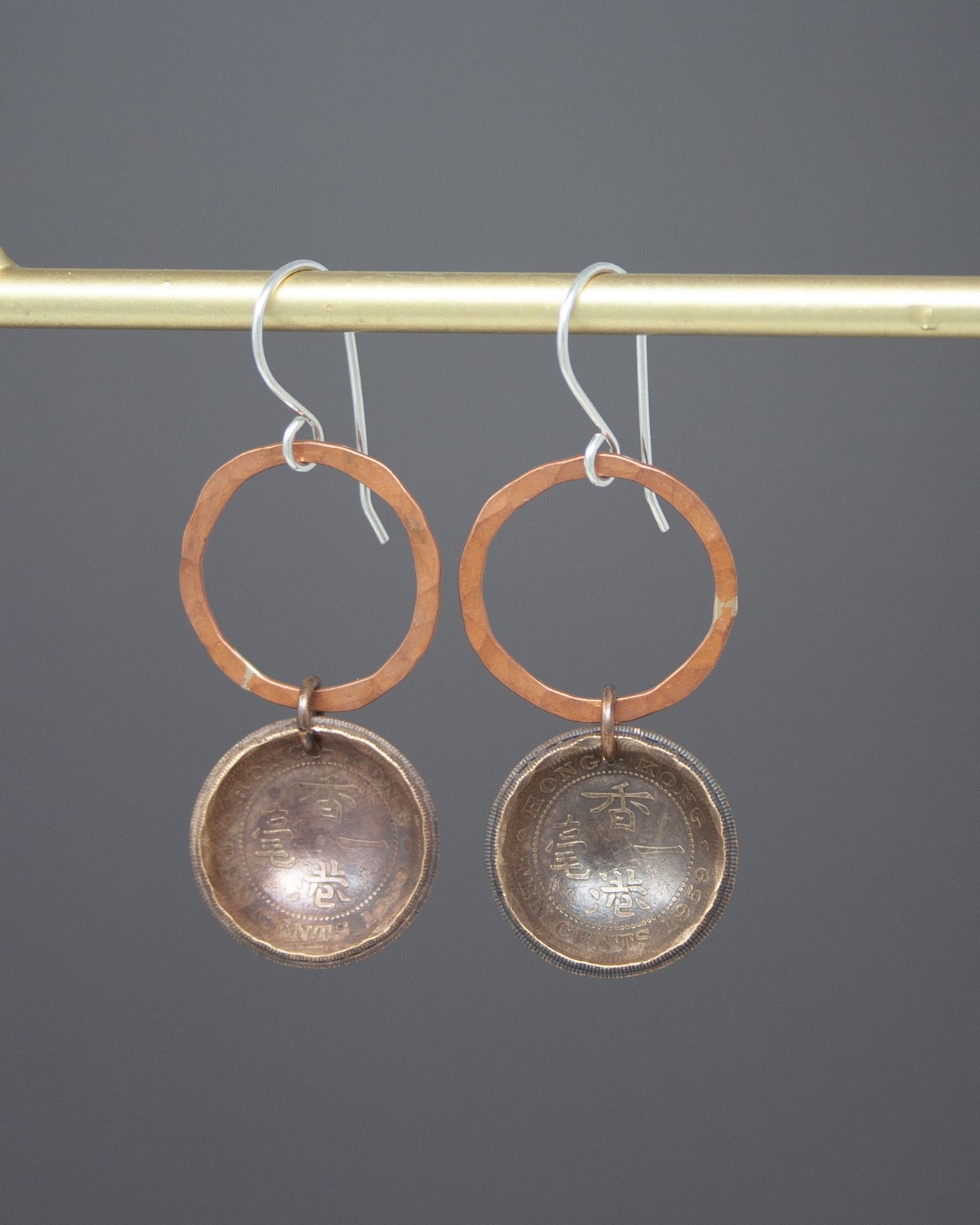 A pair of earrings with a circular design and a metal ring hanging from a hook.