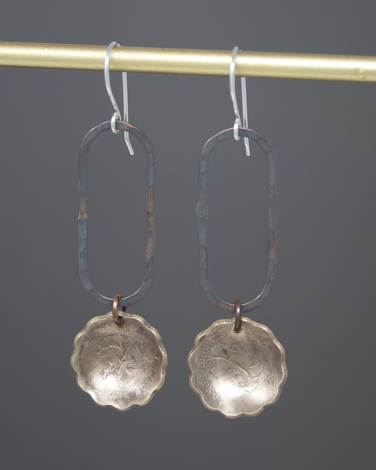 A pair of earrings with a metal frame and a metal disc-shaped pendant hanging from a hook.