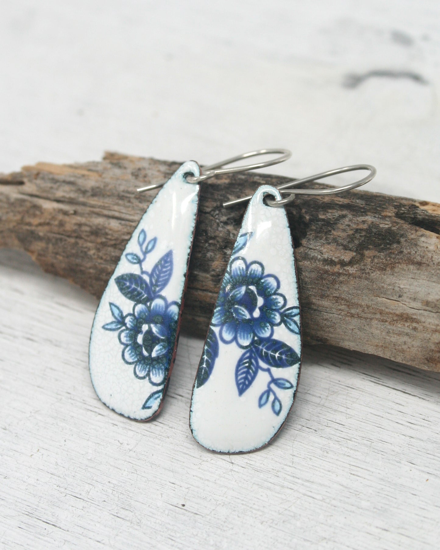 a pair of blue and white floral earrings on a piece of wood