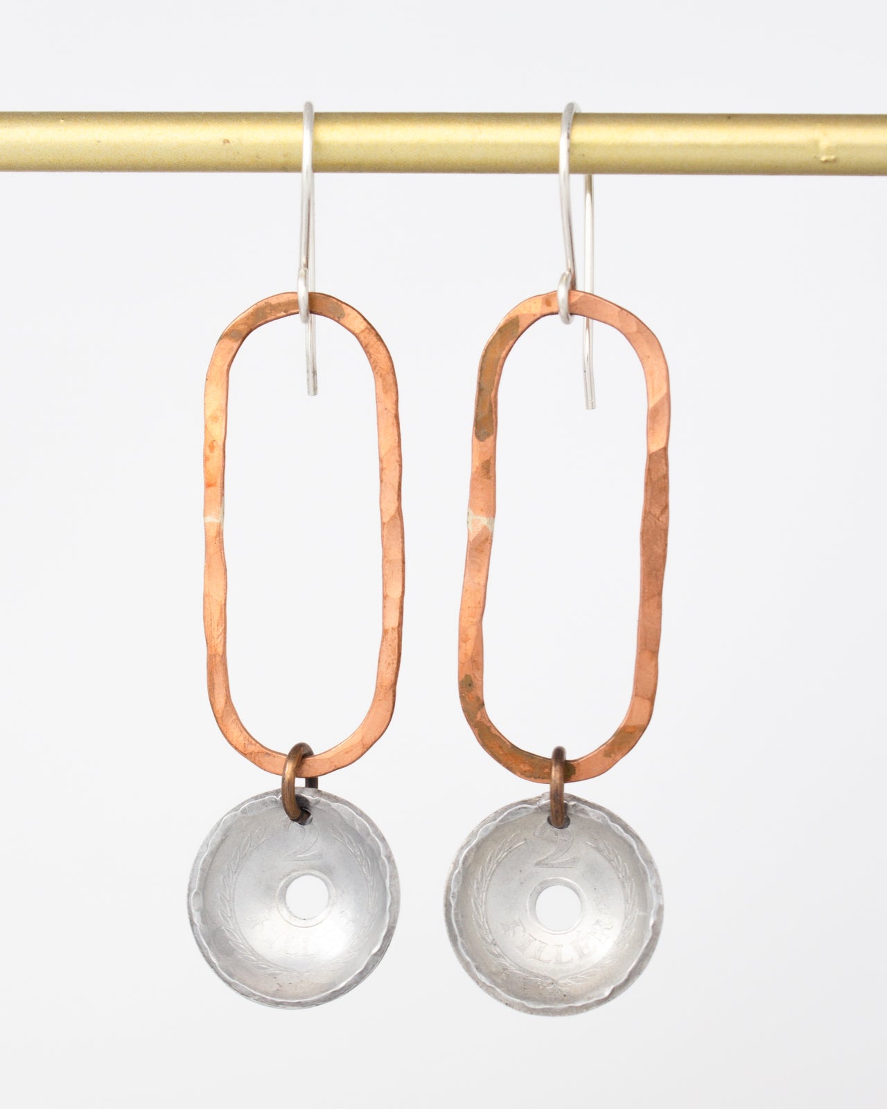A pair of earrings with a combination of copper and silver materials, featuring a circular pendant and a metallic frame.