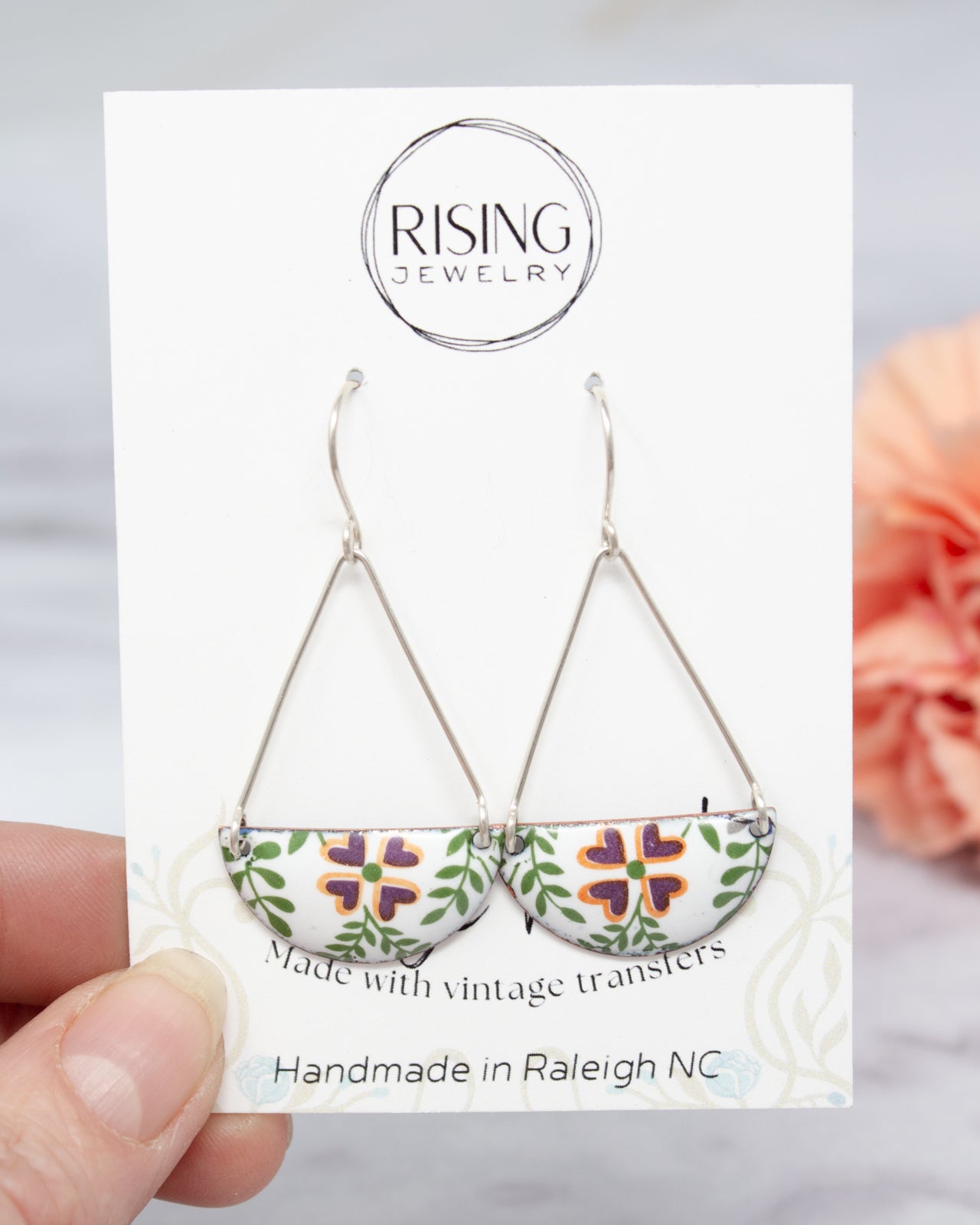 A hand holding a pair of earrings with a handmade jewelry card in front of them.