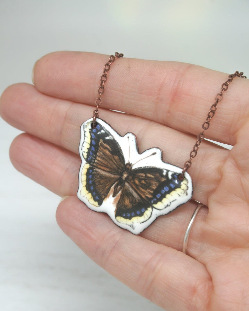 A hand holding a necklace with a butterfly pendant.