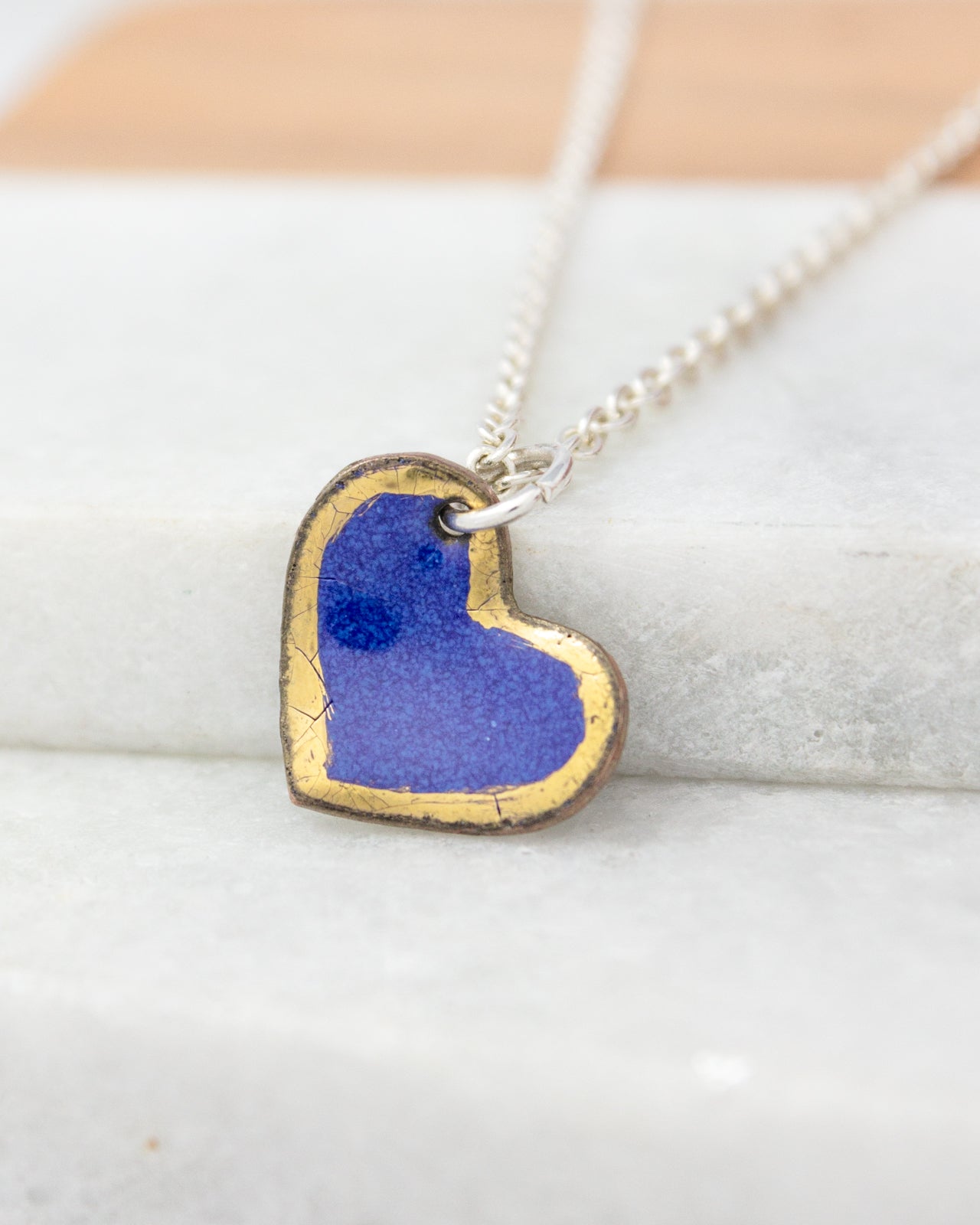 A heart-shaped pendant with a blue background and a gold border is hanging from a silver chain.