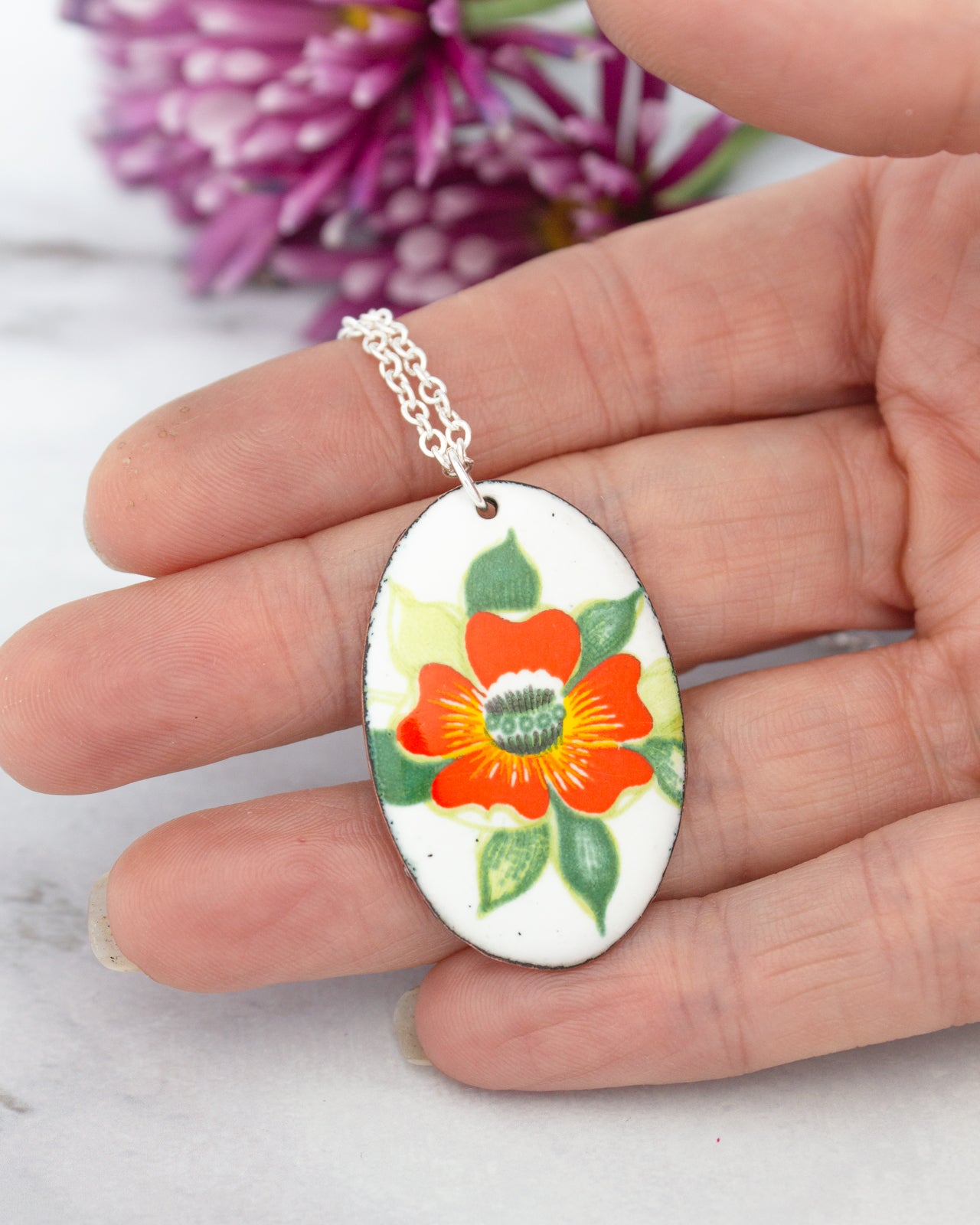 A hand holding a pendant with a colorful flower design.