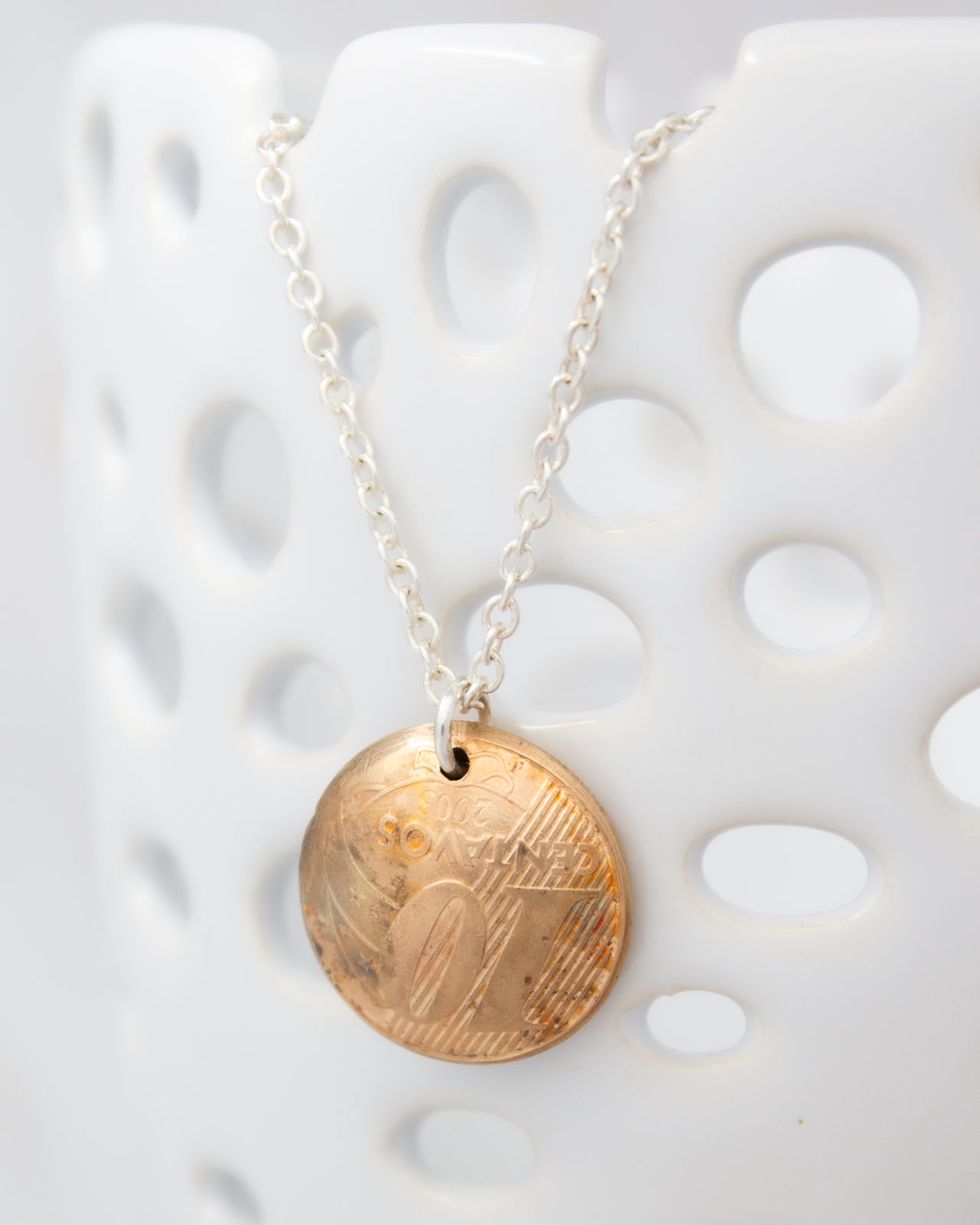 A necklace with a round pendant featuring a design, possibly a coin or a small metal object, hanging from a chain.