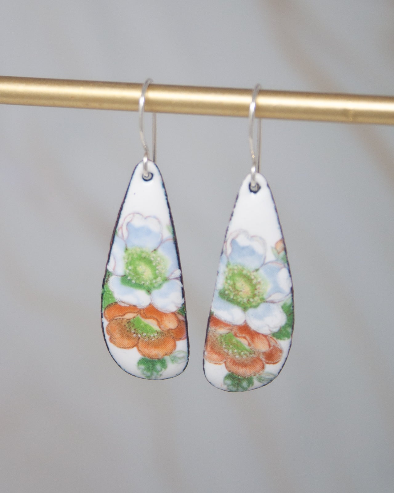 A pair of earrings with a floral design, hanging from a gold-colored metal hook.