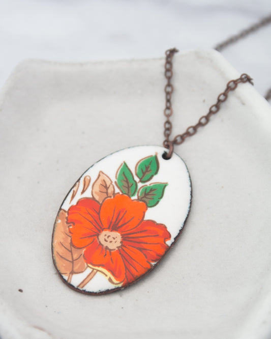 A pendant necklace with a white oval-shaped pendant featuring a vibrant red flower with green leaves.