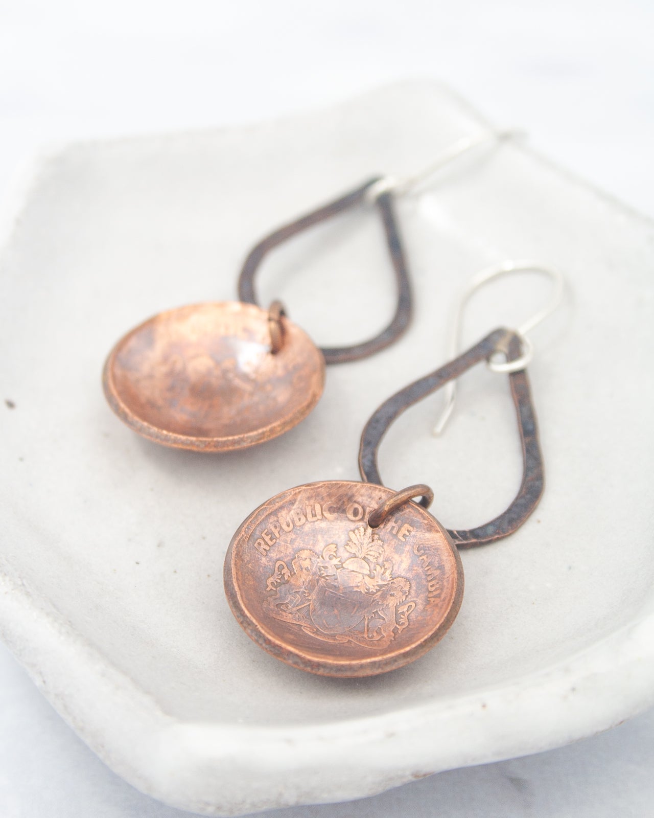 A pair of copper-colored earrings with a floral design, resting on a white surface.