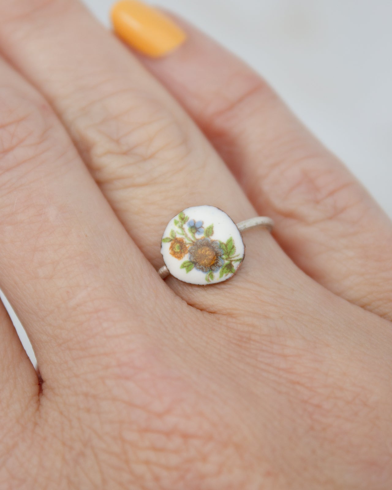 A close-up of a person's hand wearing a ring with a floral design on it.