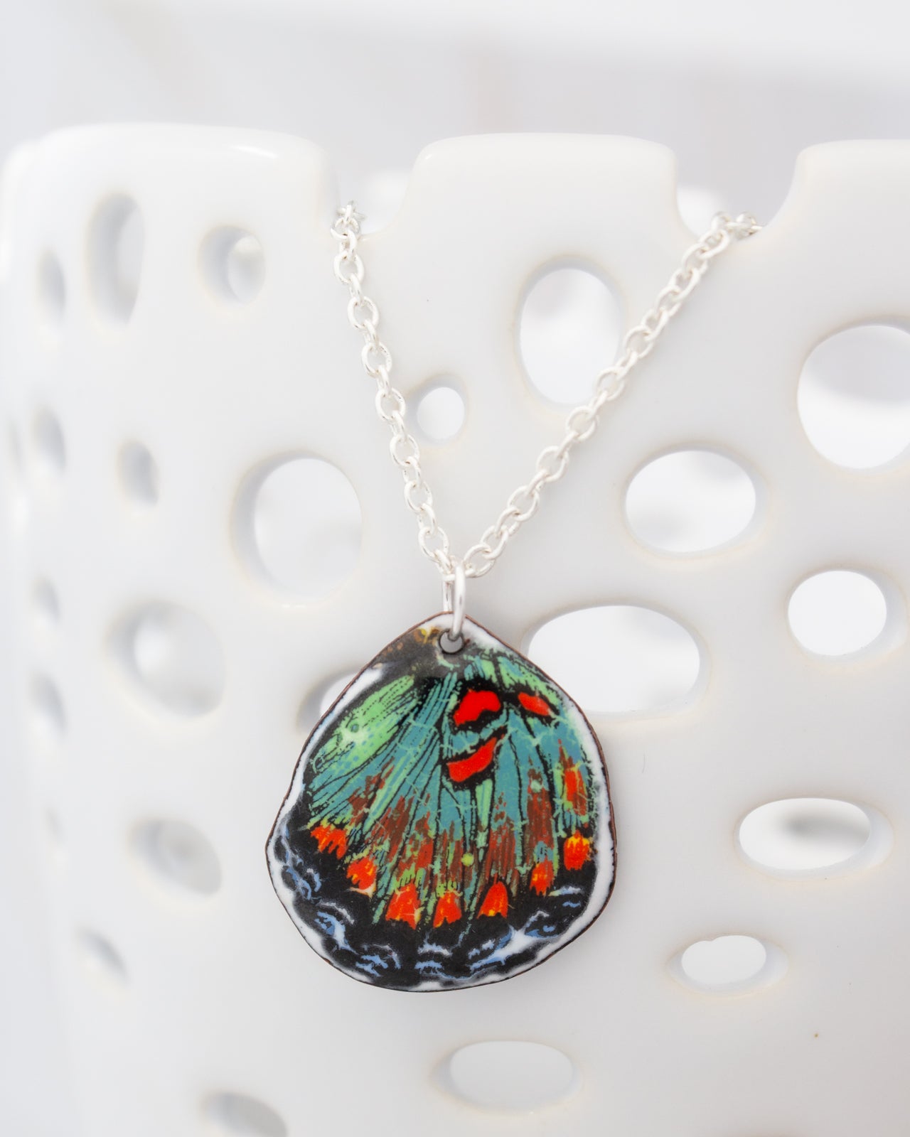 A colorful pendant necklace with a butterfly design is displayed against a white background.