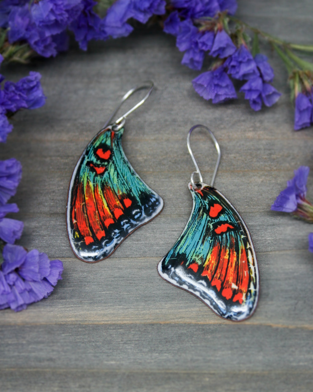 a pair of butterfly shaped earrings sitting next to purple flowers