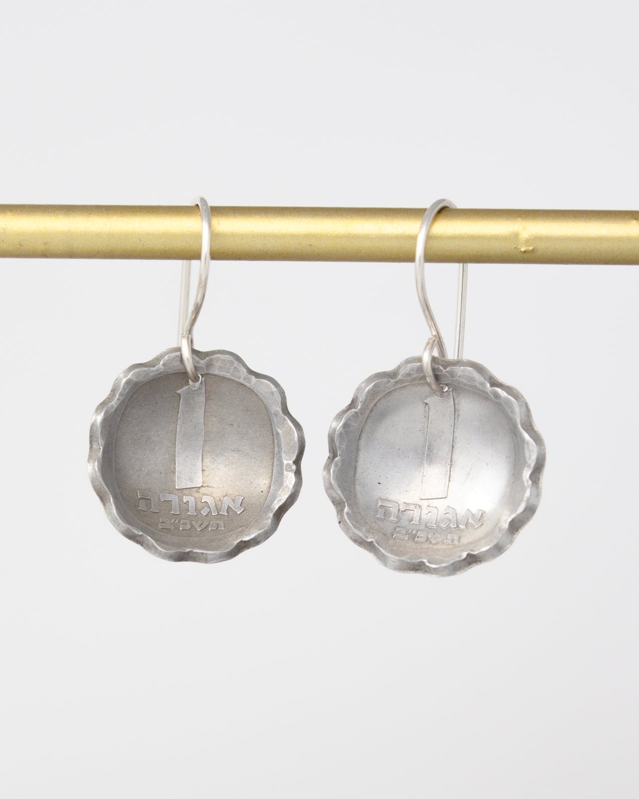 a pair of silver earrings hanging from a gold bar.