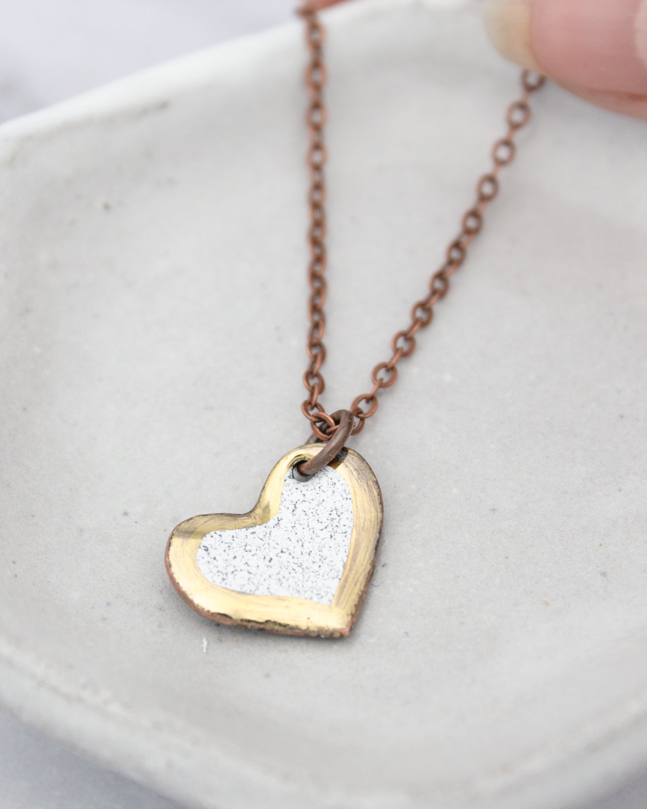 A delicate heart-shaped pendant necklace with a silver and gold color scheme, resting on a white surface.