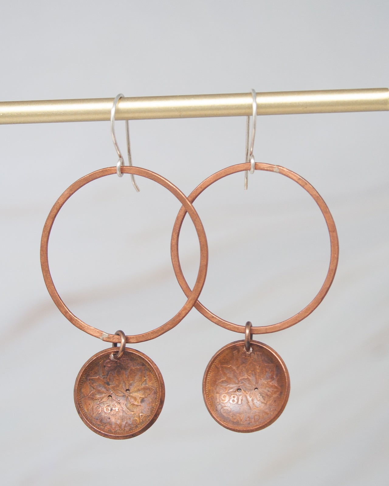 A pair of copper-colored earrings with circular pendants hanging from a gold-colored metal hook.