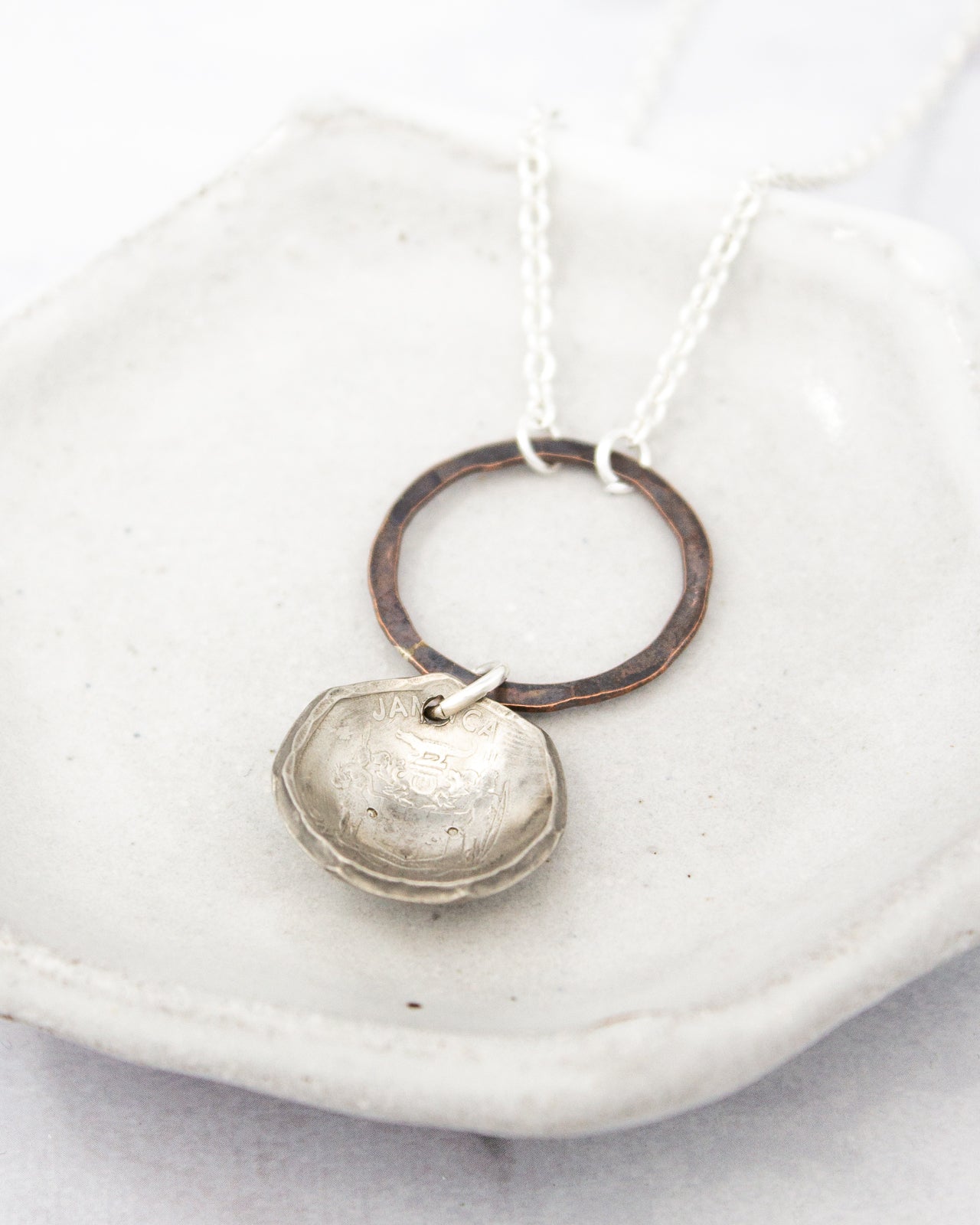 A silver necklace with a round pendant and a circular metal ring hanging from it, resting on a white surface.