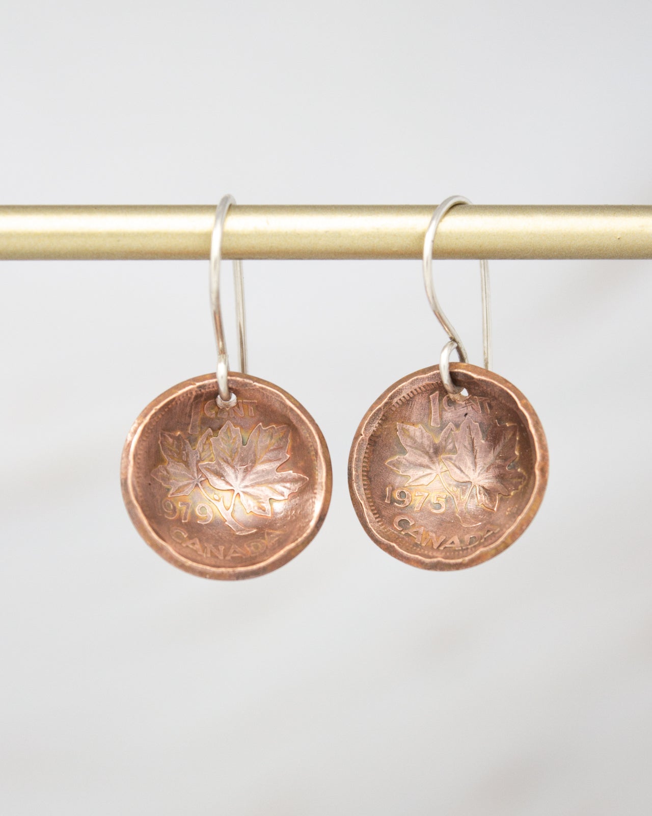 A pair of copper-colored earrings with leaf designs, hanging from a gold-colored metal hook.