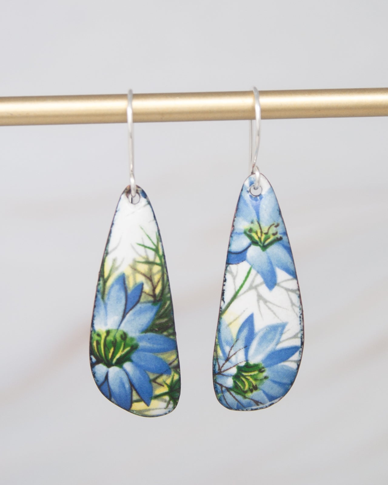 A pair of earrings with blue floral designs hanging from a gold-colored metal bar.