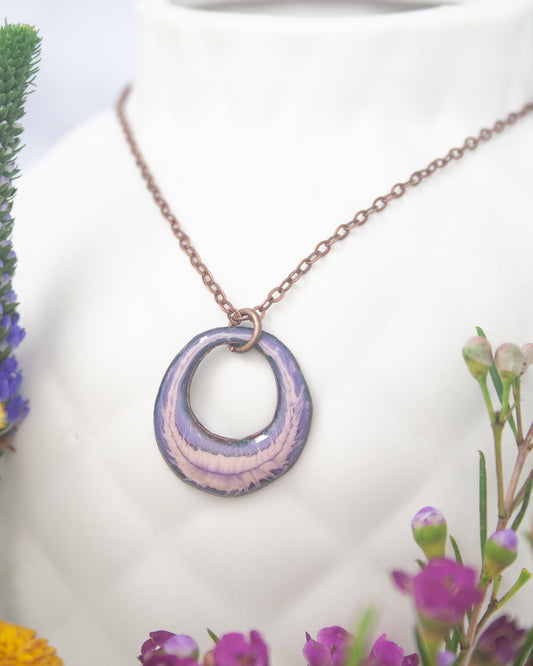 A necklace with a purple pendant is displayed against a white background, surrounded by colorful flowers.
