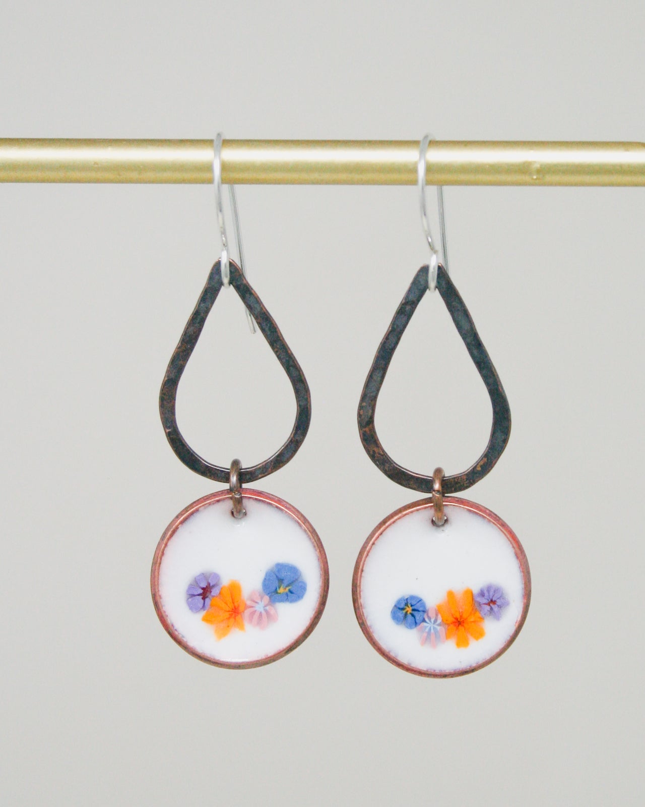 A pair of earrings with a floral design on the circular pendants hanging from a gold-colored metal hook.