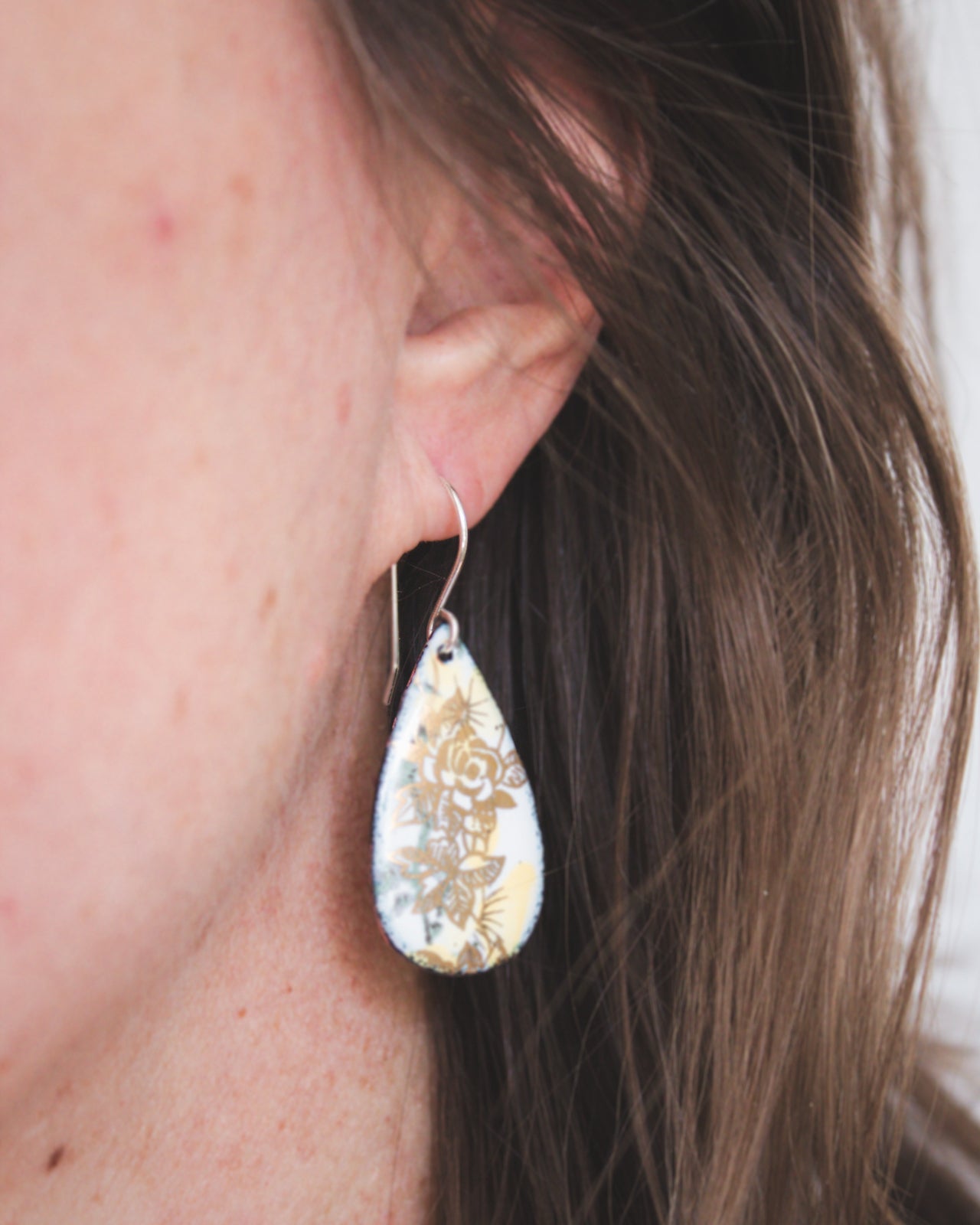 A close-up view of a person's ear wearing a pair of earrings with a floral design.