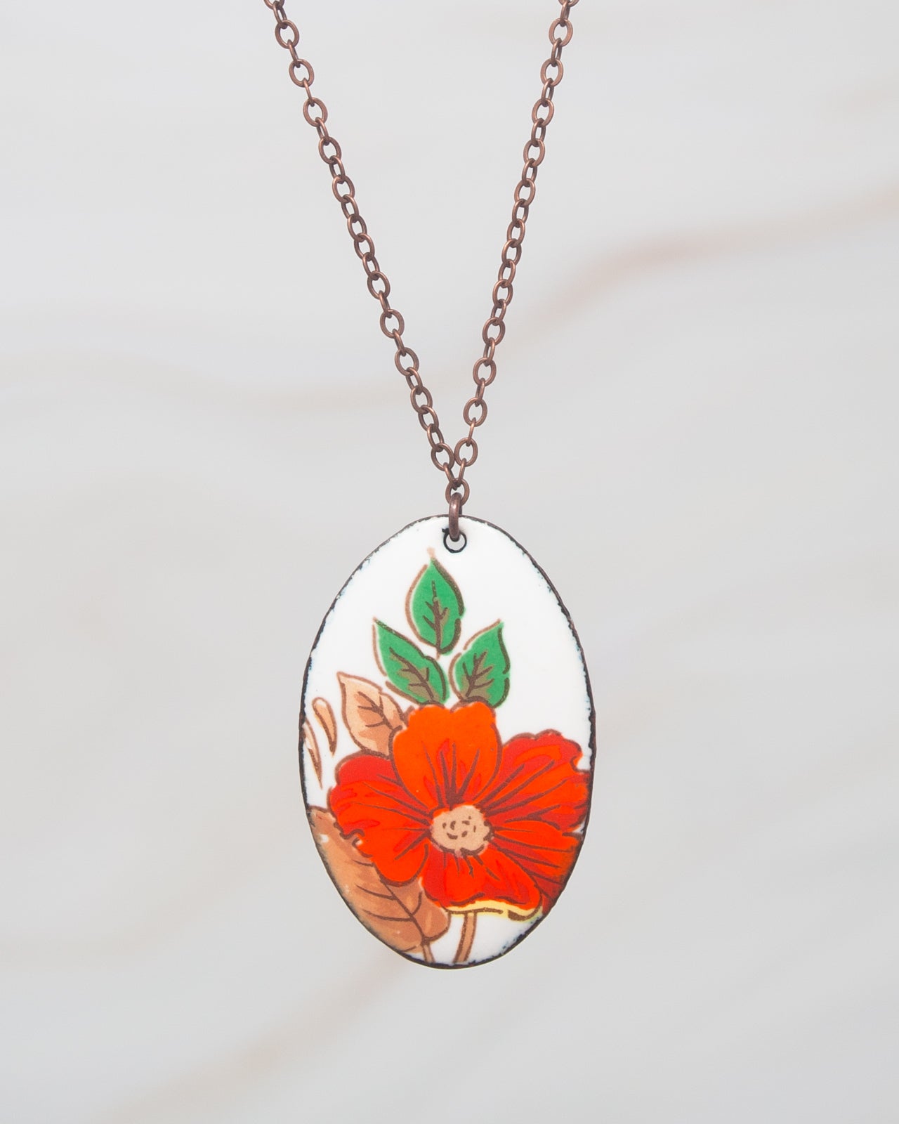 A necklace with a pendant featuring a red flower and green leaves.