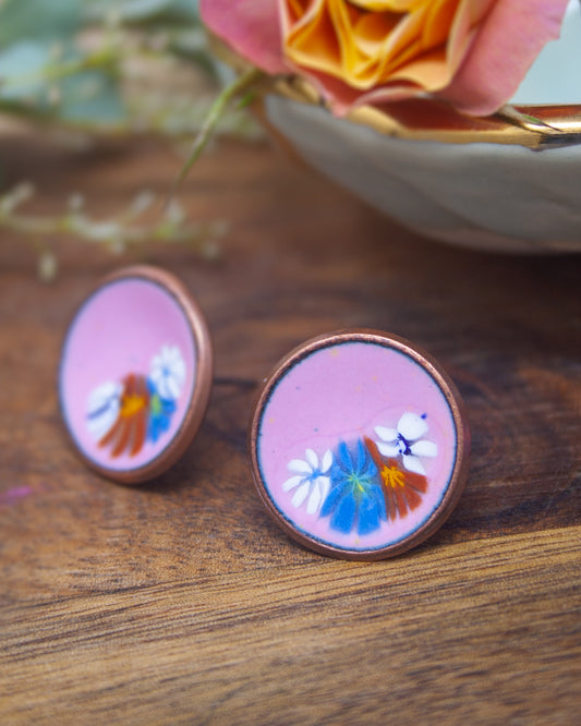 two round, copper-colored earrings with a floral design on them, placed on a wooden surface.