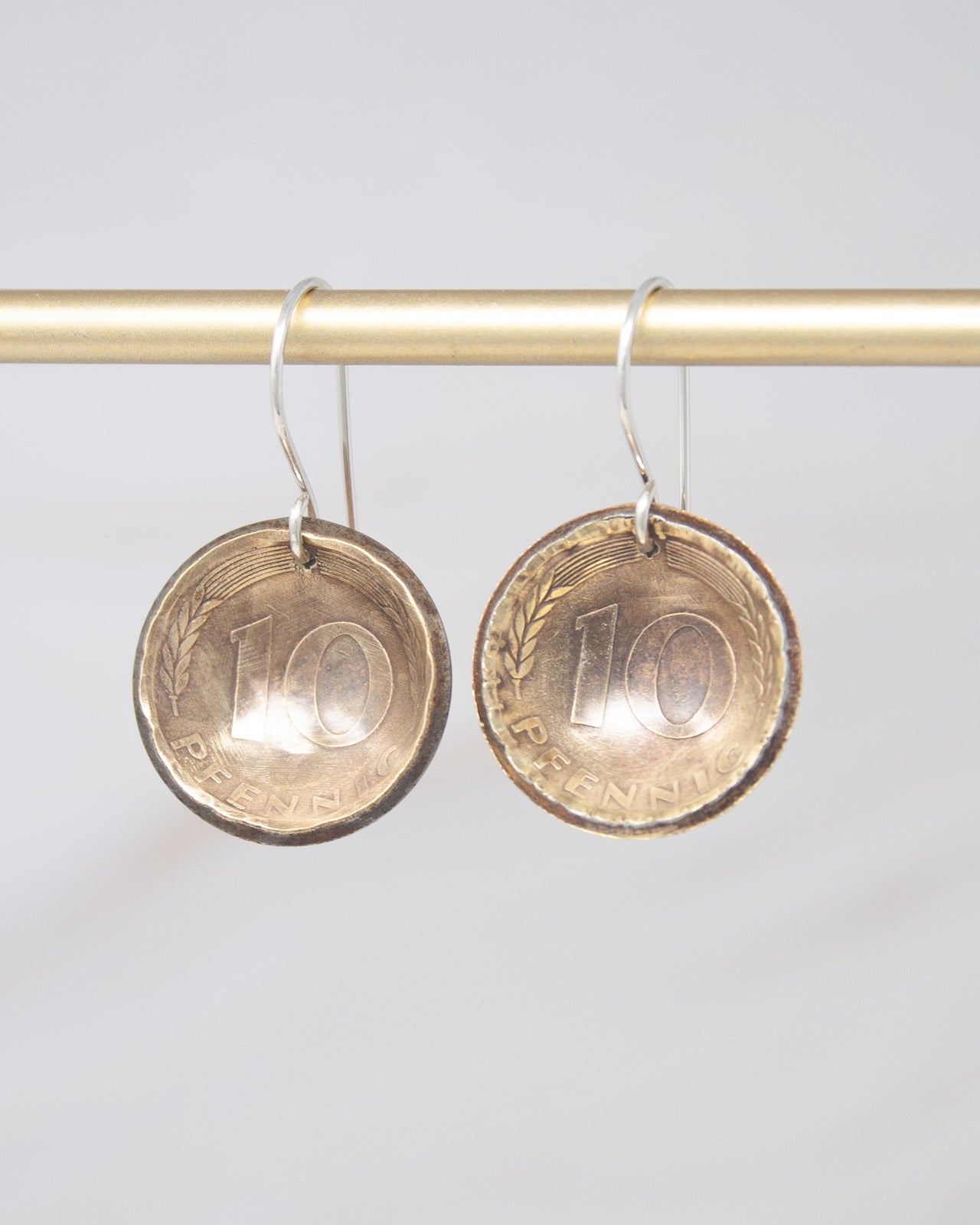 A pair of earrings made from a 10 pence coin, hanging from a gold-colored metal hook.