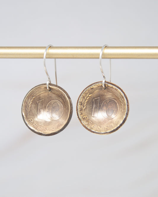A pair of earrings made from a 10 pence coin, hanging from a gold-colored metal hook.