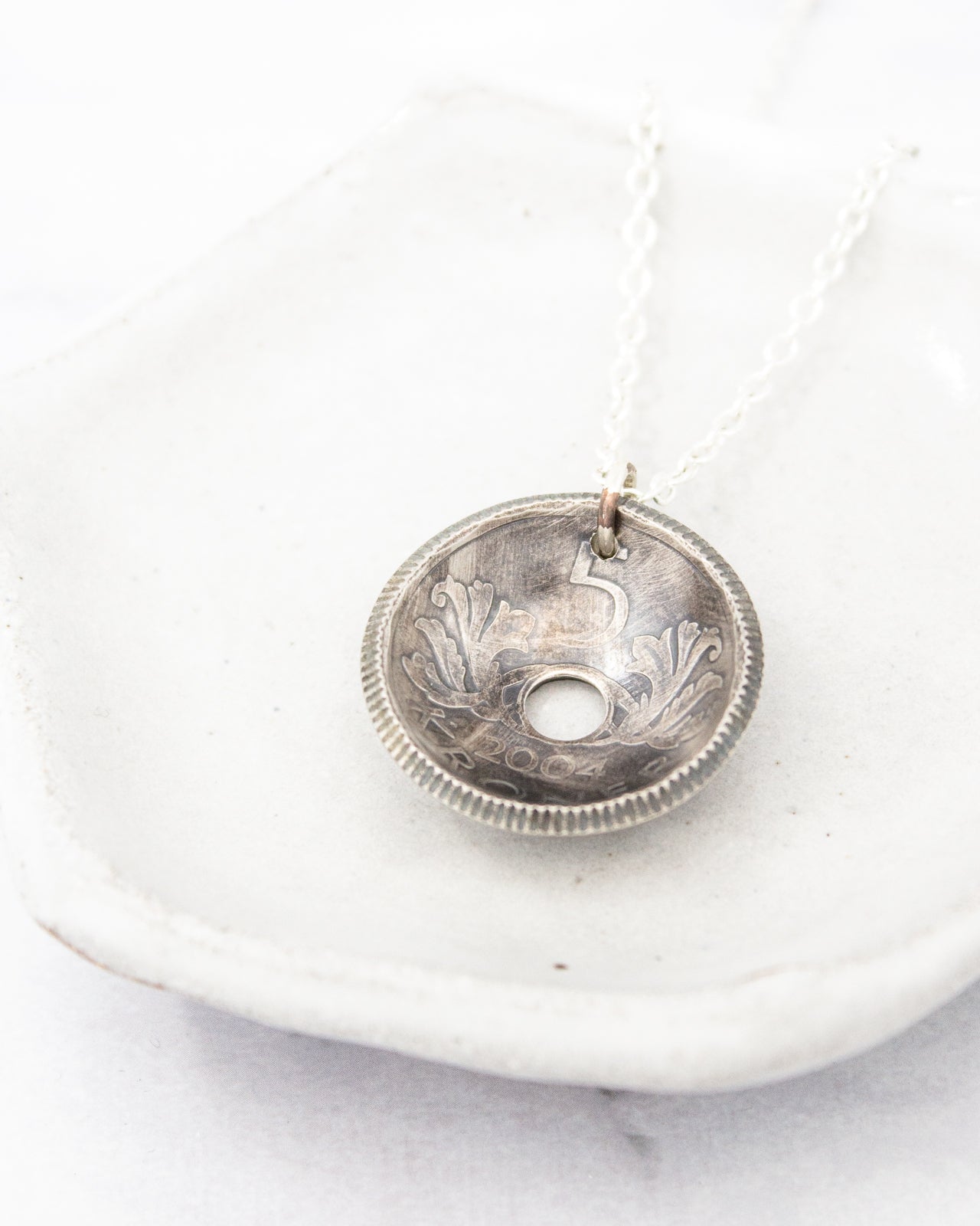 A silver pendant necklace with a circular pendant featuring an embossed design.