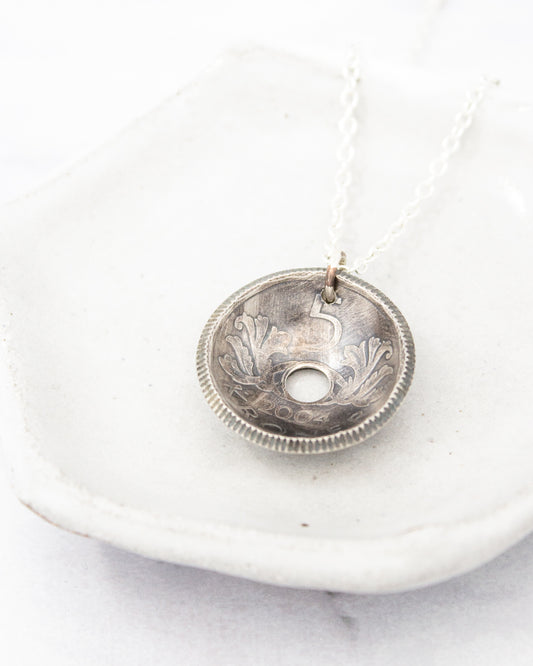 A silver pendant necklace with a circular pendant featuring an embossed design.