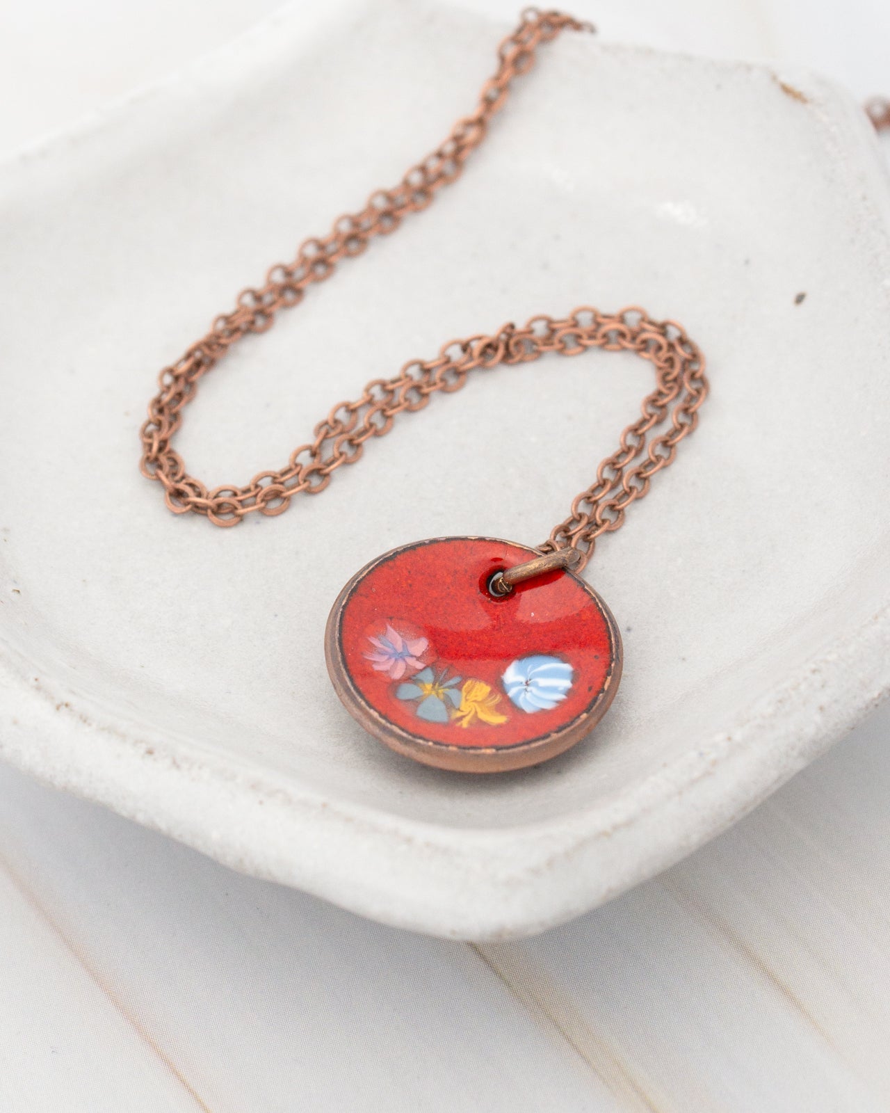 A round pendant with a red background and colorful flowers is displayed on a white plate.