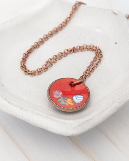 A round pendant with a red background and colorful flowers is displayed on a white plate.