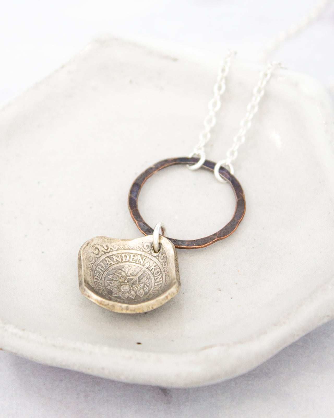 A silver necklace with a pendant featuring a floral design, resting on a white surface.