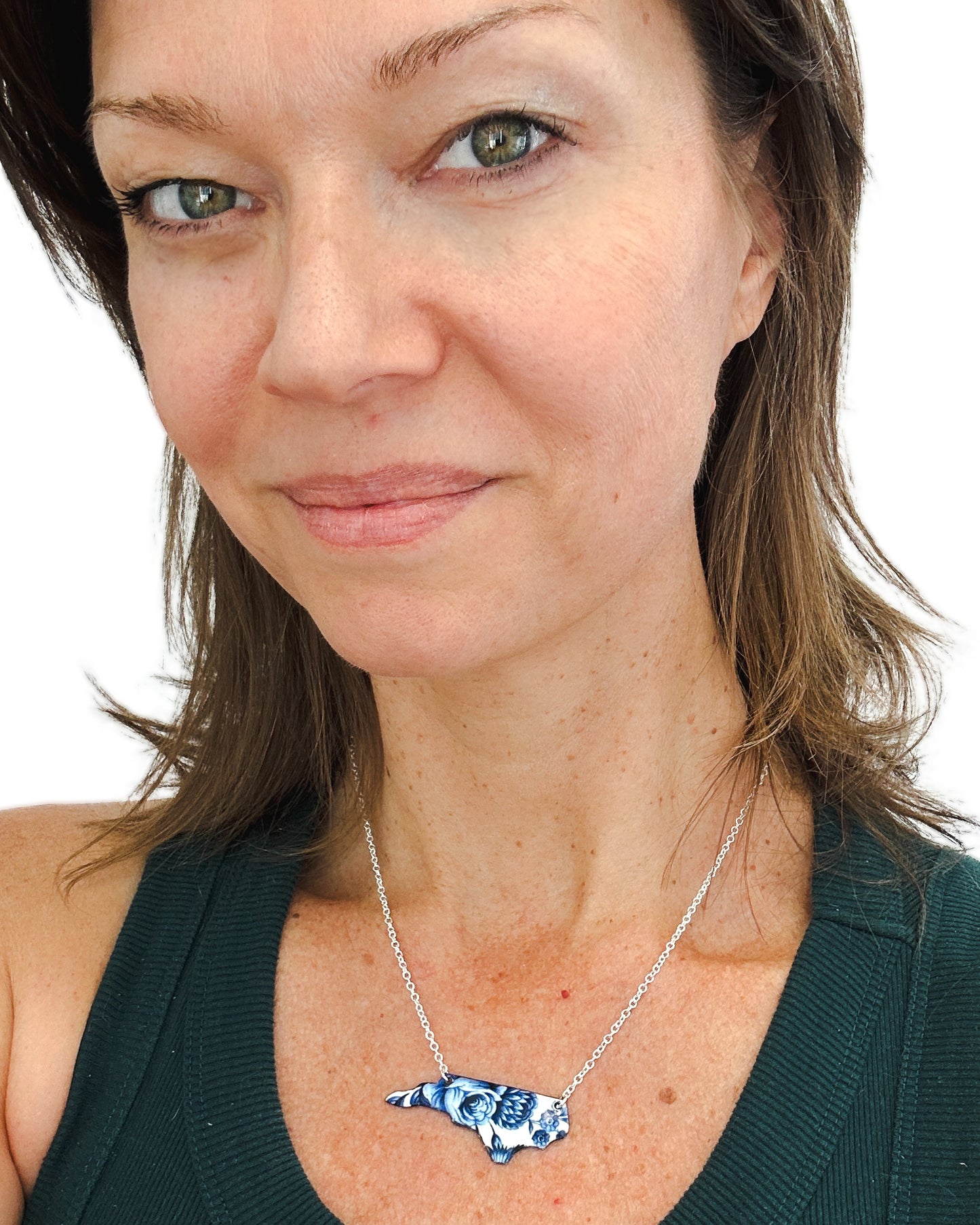 A woman wearing a green top and a necklace with a blue and white floral pendant.