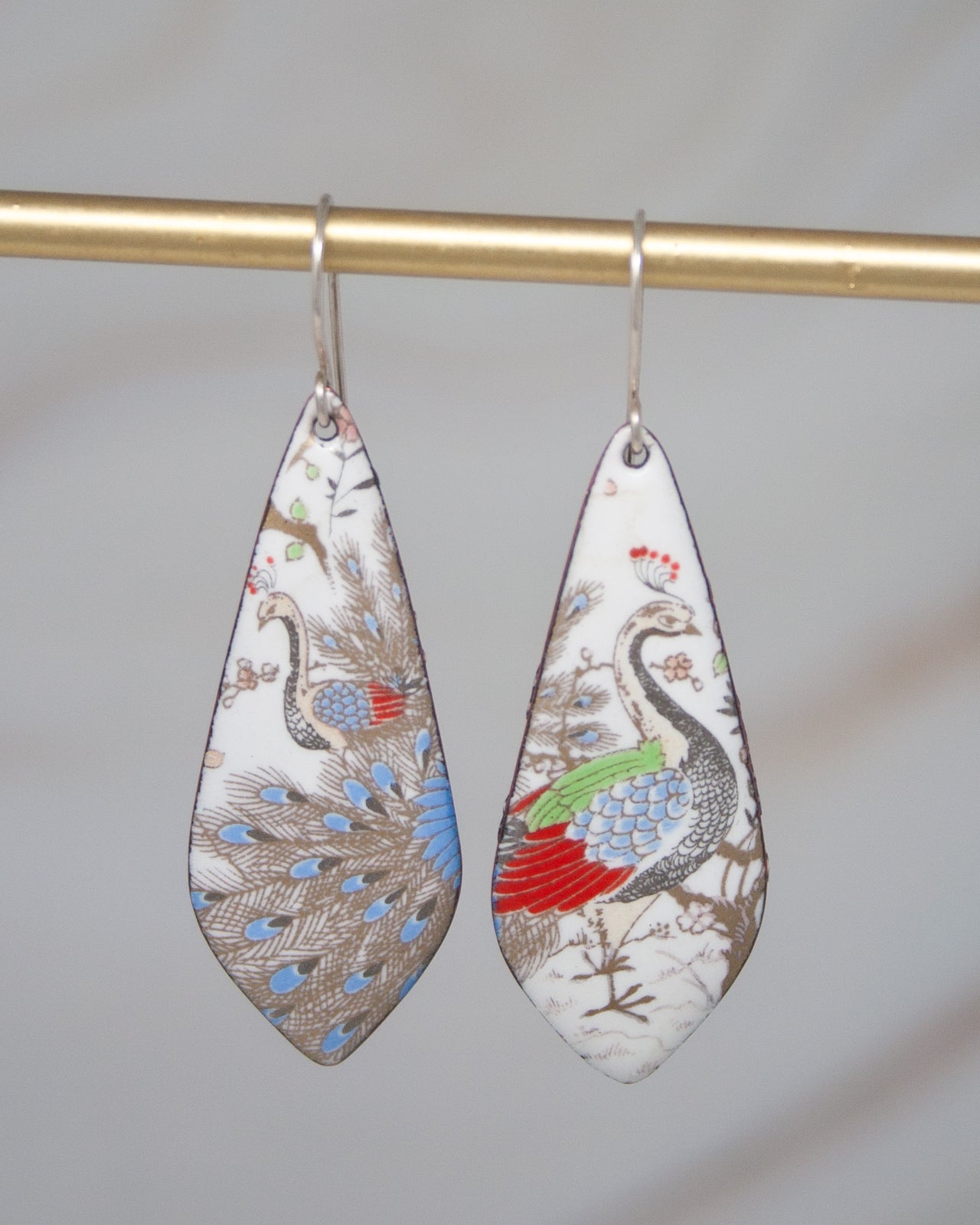 A pair of earrings with a colorful, intricate design featuring a peacock and other birds.