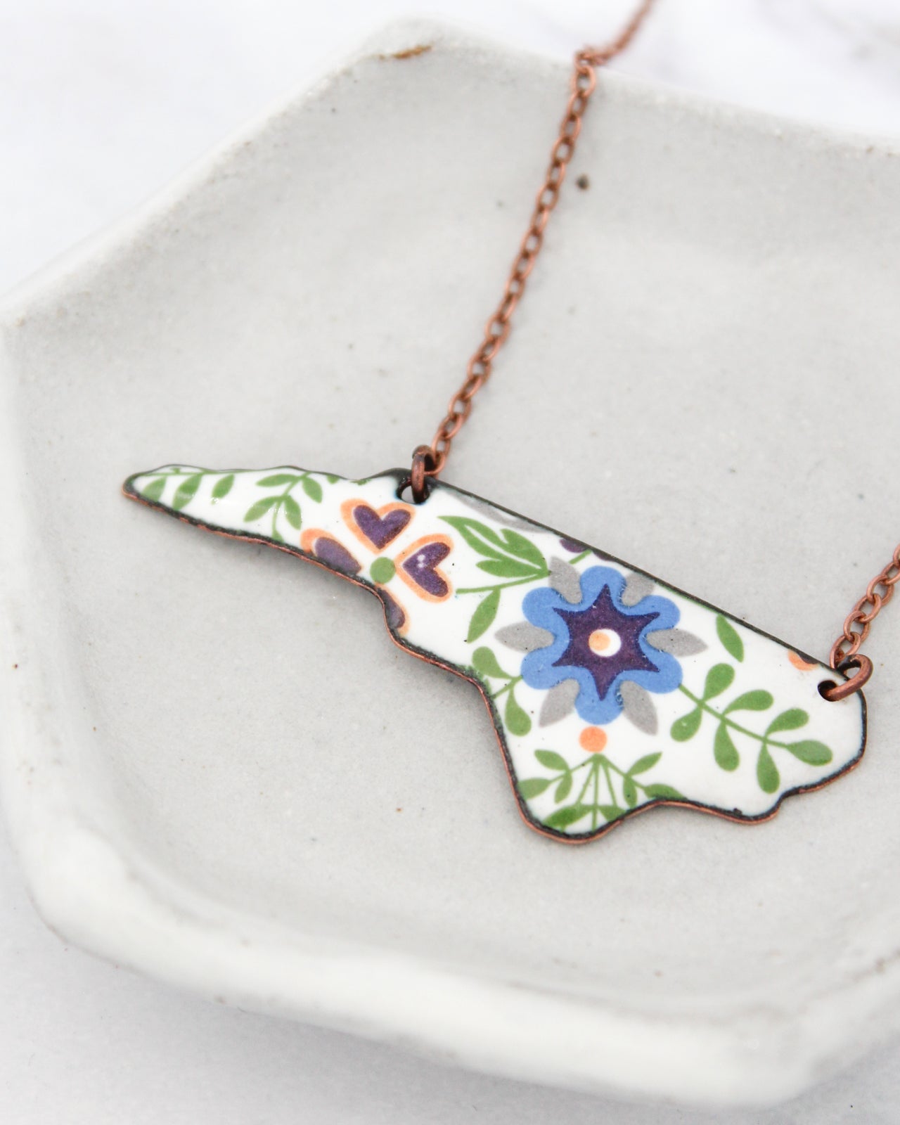 A necklace with a pendant in the shape of a flower, featuring a blue center and green leaves.