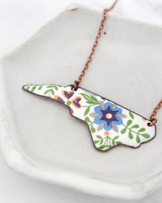 A necklace with a pendant in the shape of a flower, featuring a blue center and green leaves.