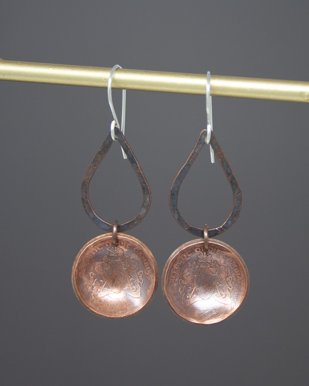 A pair of copper-colored earrings with a circular design hanging from a hook.