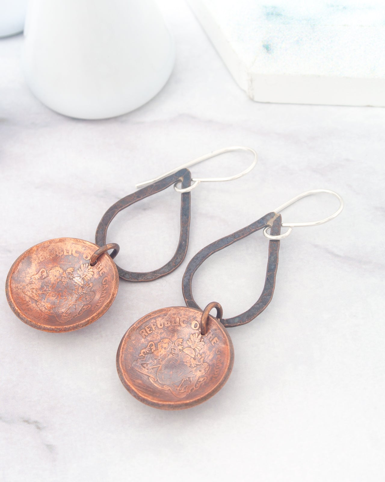 A pair of copper-colored earrings with a floral design, resting on a white marble surface.