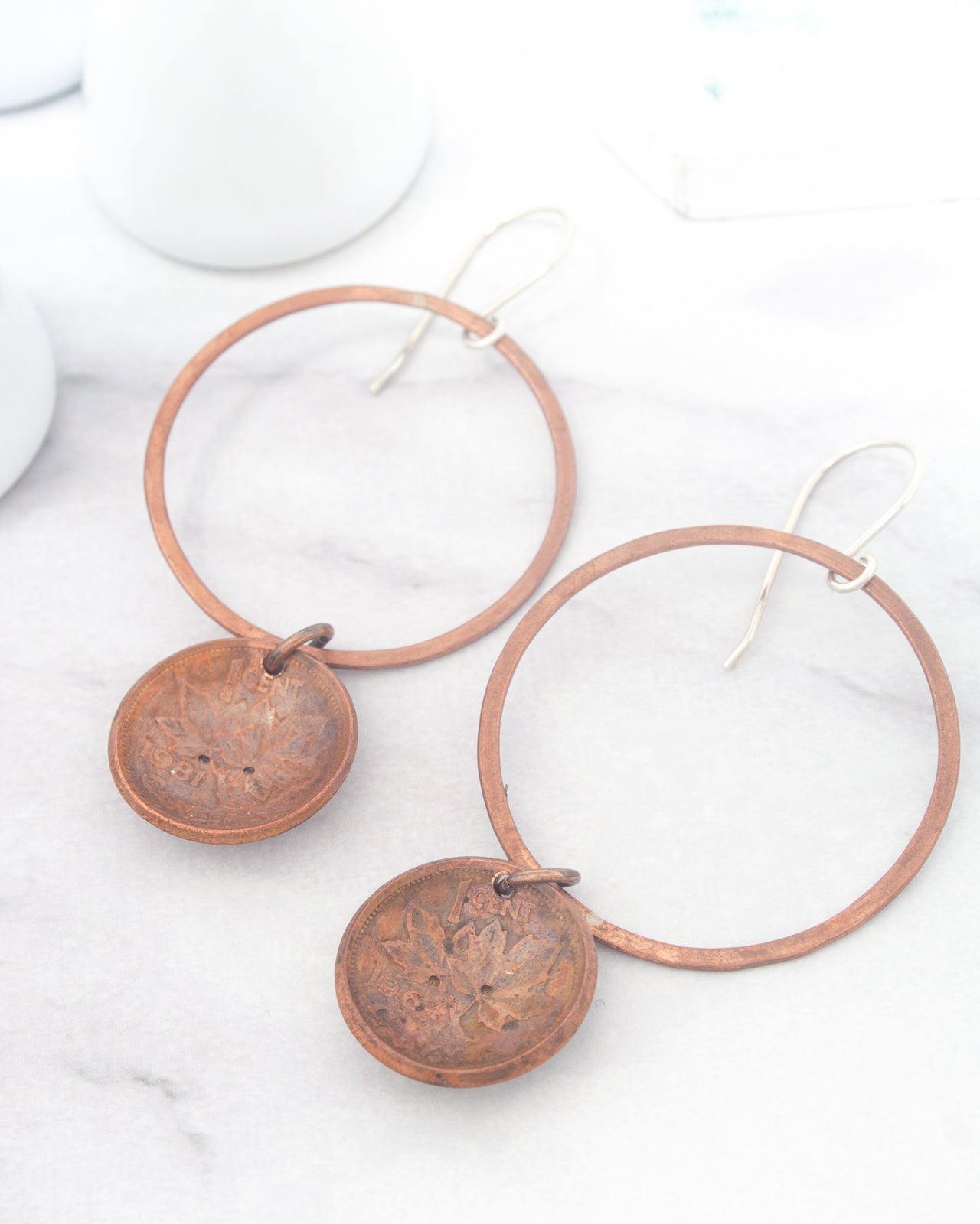 A pair of copper-colored earrings with circular pendants hanging from the ear hooks, resting on a white marble surface.